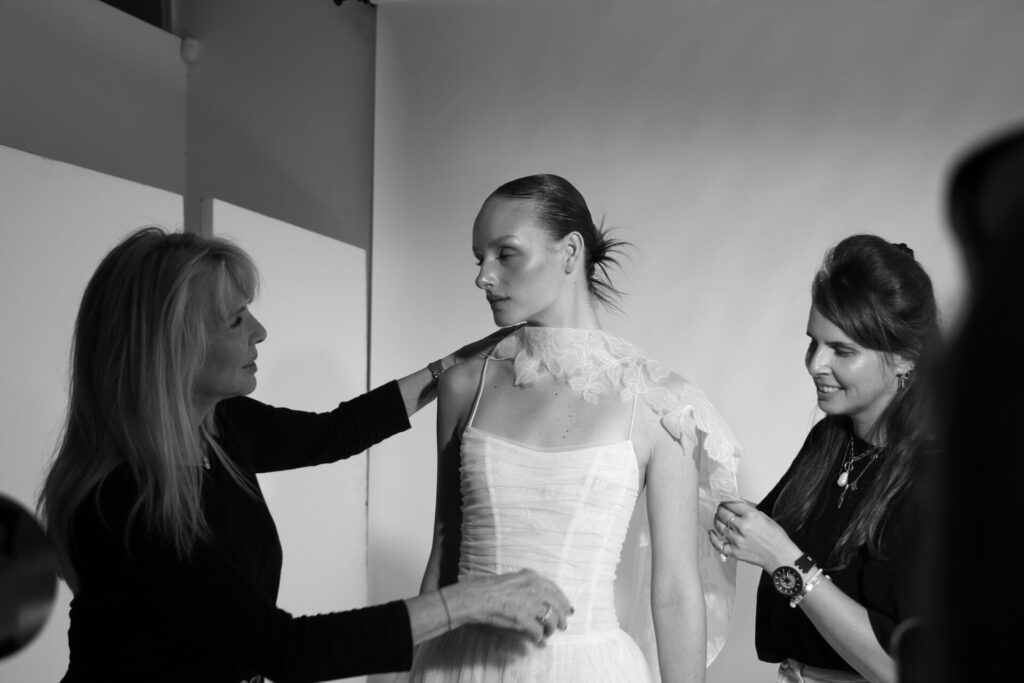 Women fix floral shoulder detail on model.