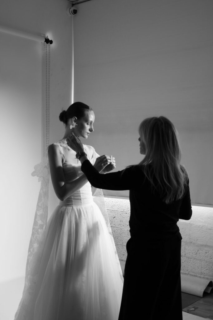 Black and white: bride stands, dress adjusted.