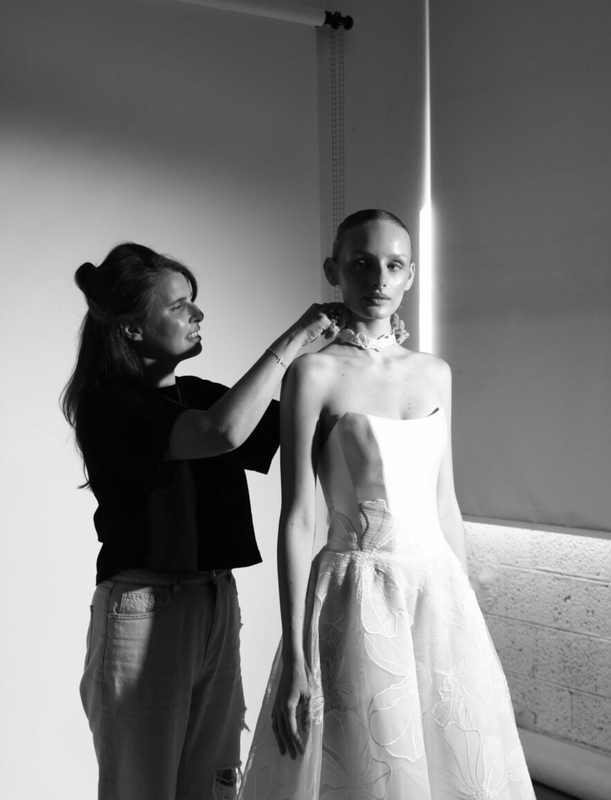 Woman adjusts necklace on model in studio.