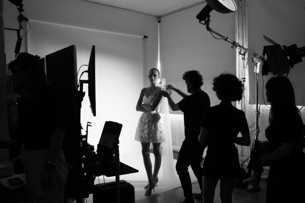 Model posing as stylist adjusts dress, silhouettes foreground.