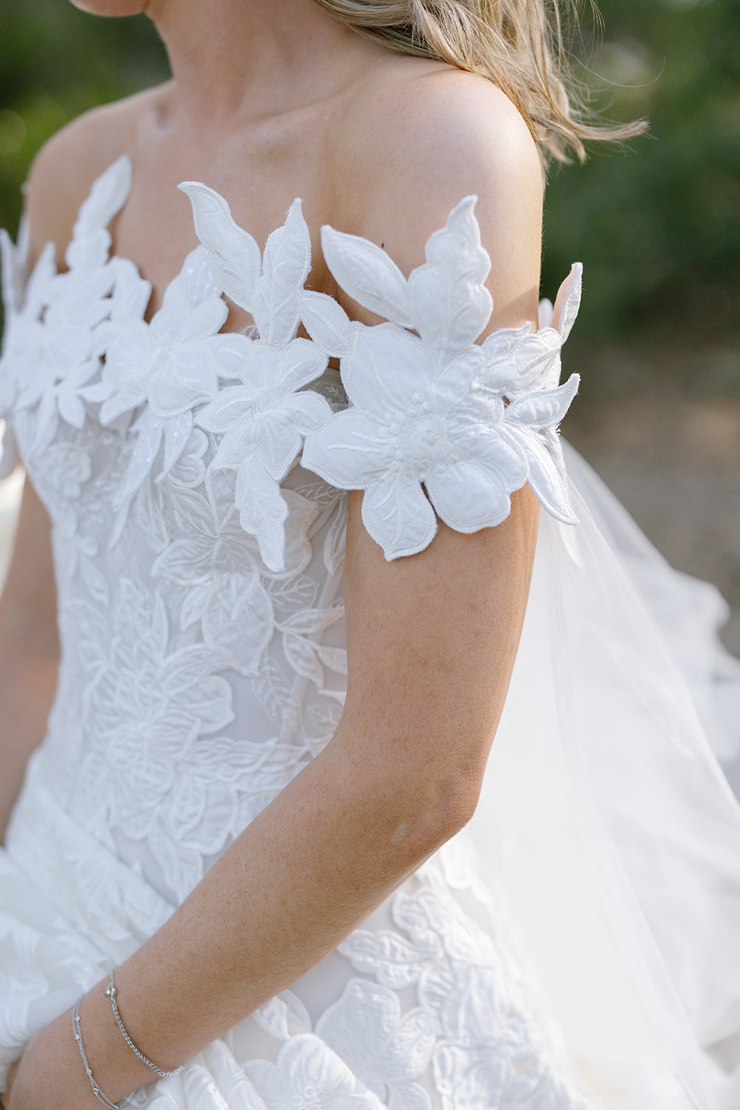 Woman in floral white wedding dress outdoors, loose hair.