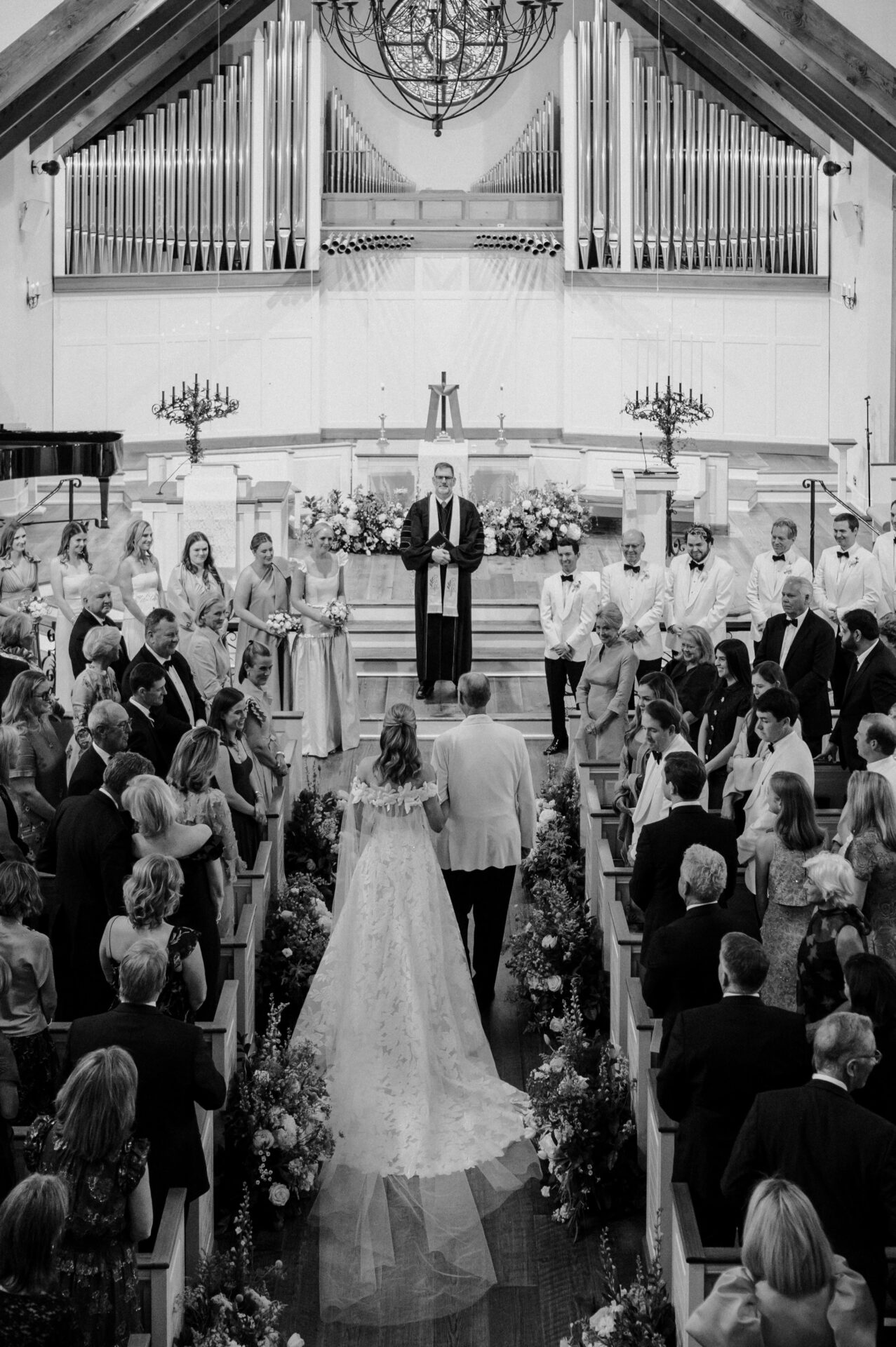 Bride and father walk down crowded aisle, black and white.