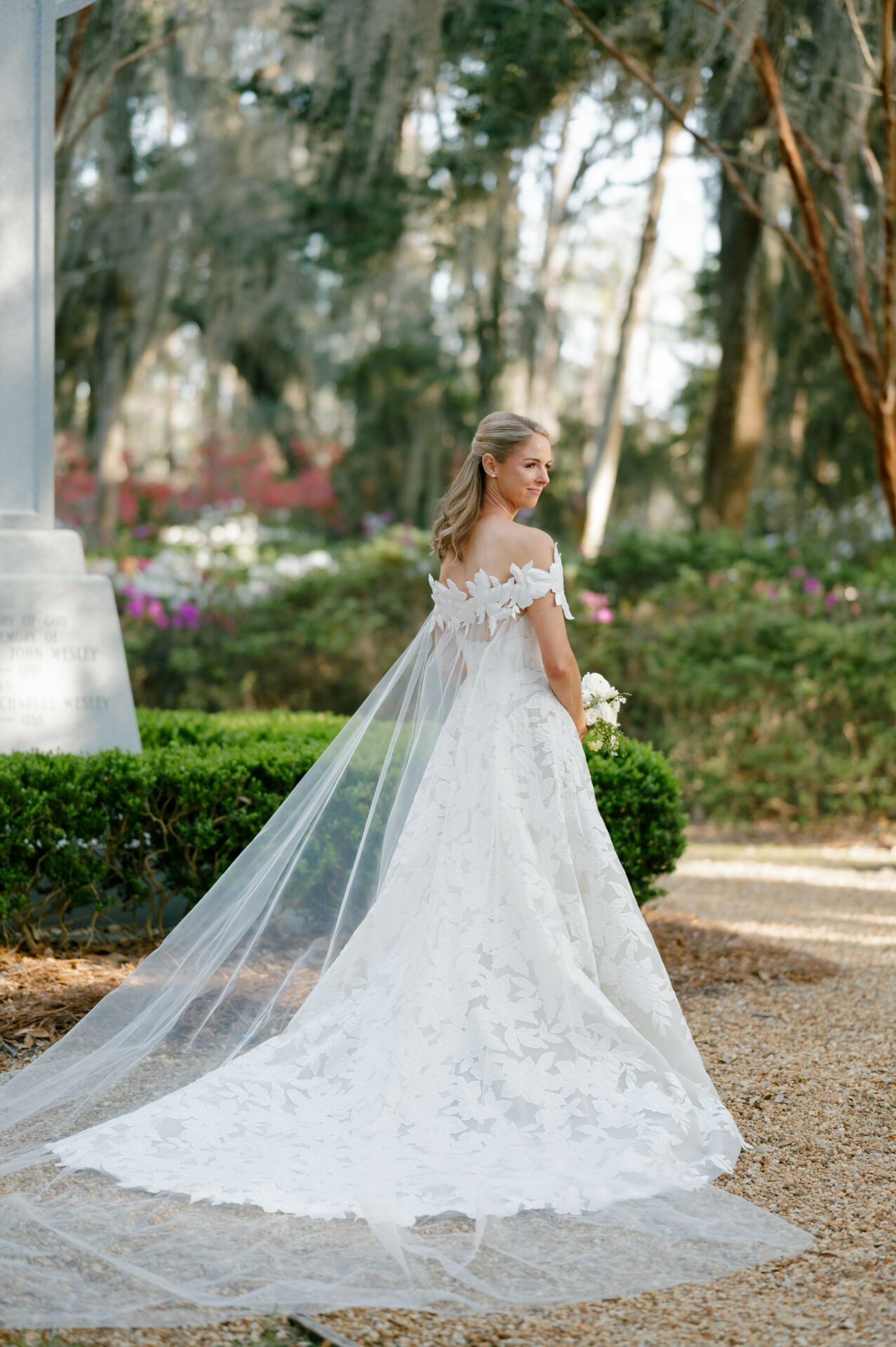 Bride in off-shoulder gown and veil in garden.