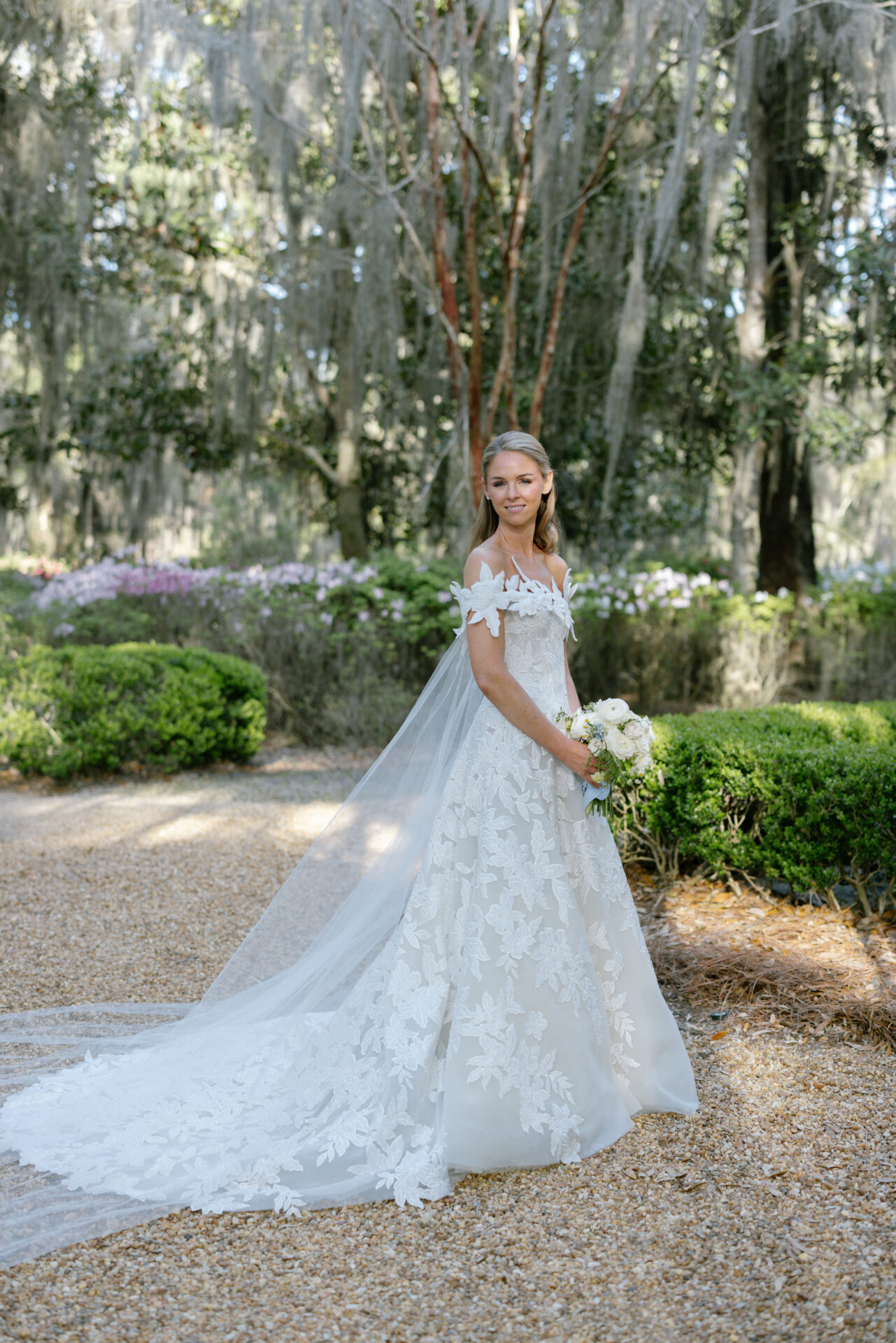 Bride in lace gown with bouquet on garden path.