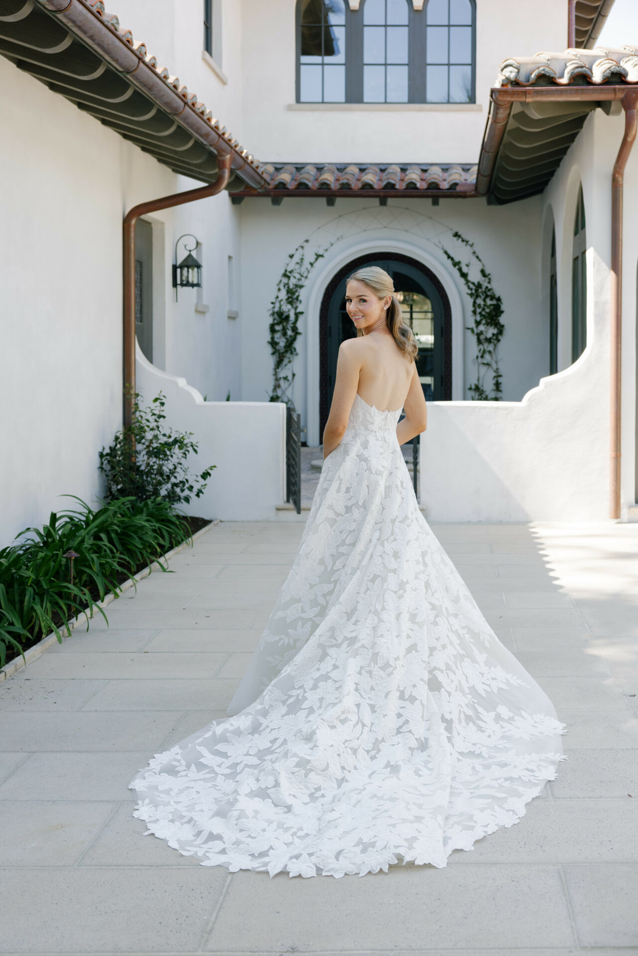 Bride in white lace gown looks back outdoors.
