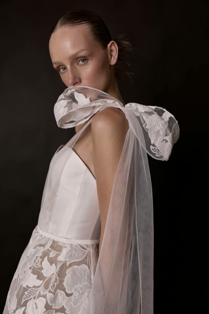 Woman in sheer floral gown with shoulder bow.