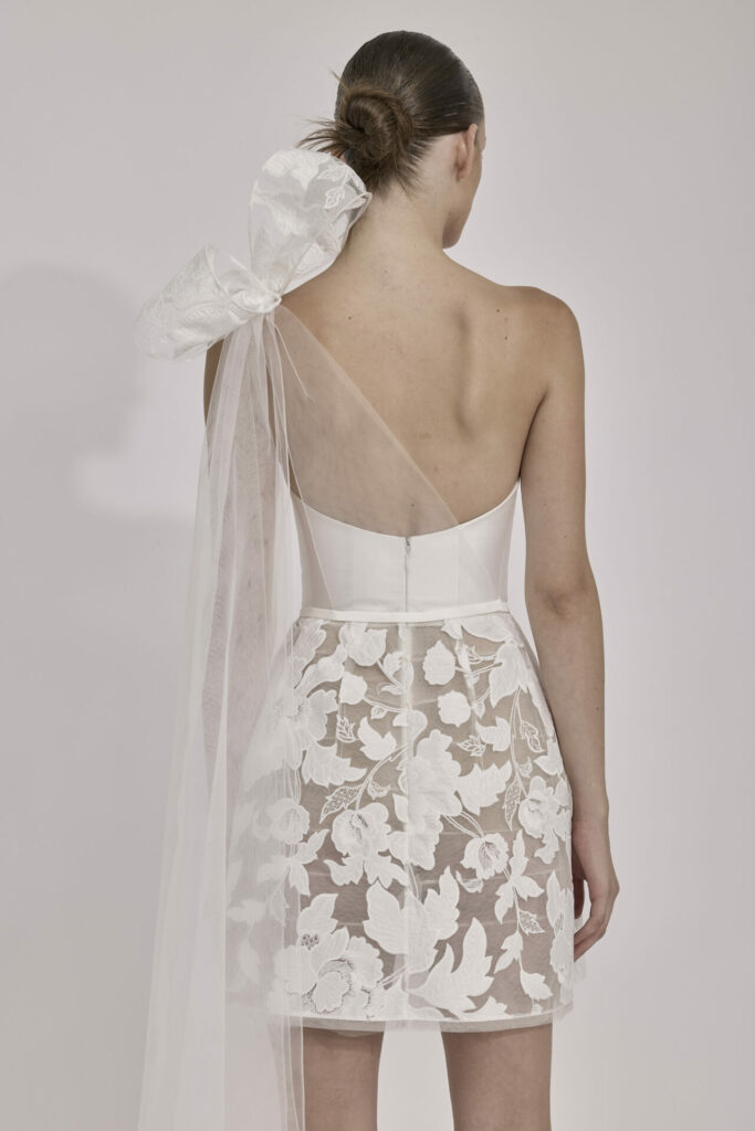 Woman in white one-shoulder dress, sheer lace skirt.