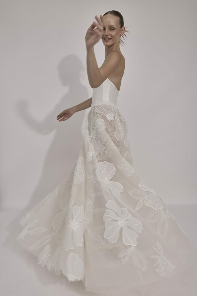 Smiling woman twirls in a floral strapless bridal dress.
