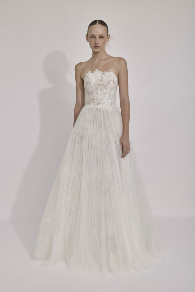 Woman in strapless white lace gown, plain background.