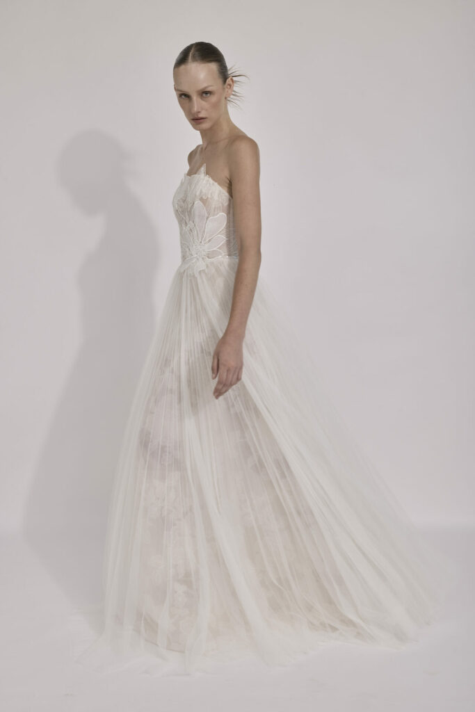 Woman in embroidered strapless white gown faces camera.