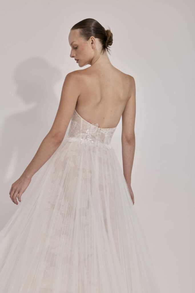 Woman in white tulle gown faces away, looking back.