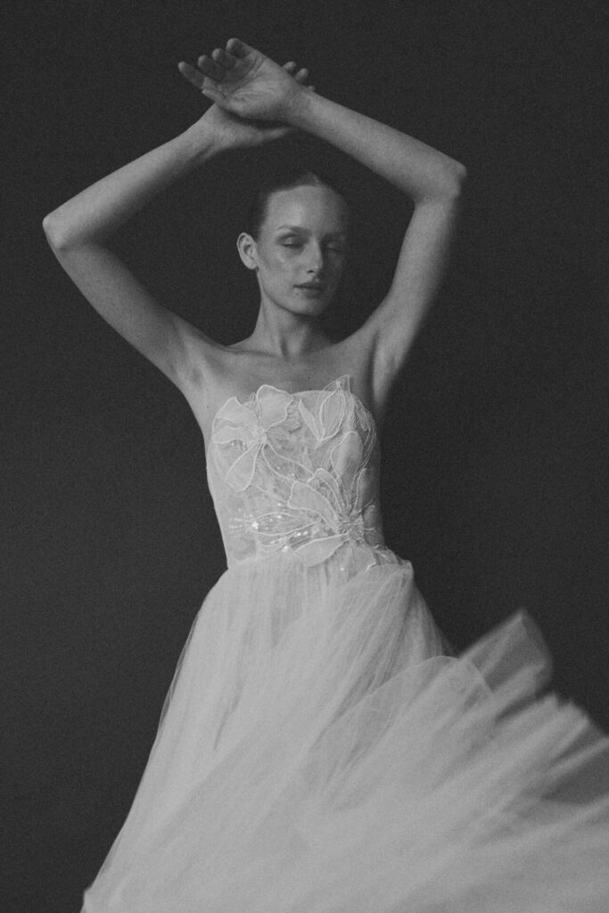 Bride in embroidered tulle dress poses dreamily, arms raised.