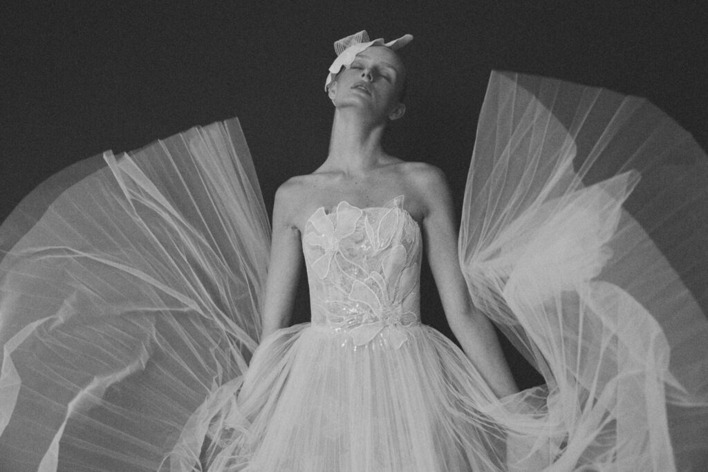 Person in ornate tulle gown, eyes closed, monochrome.