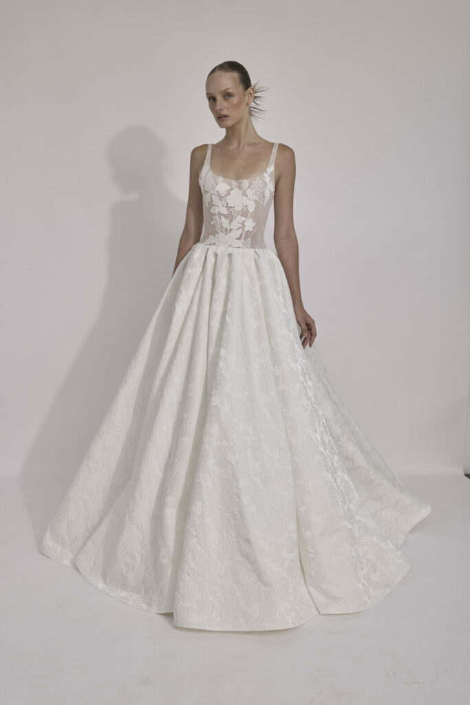 Woman in lace white wedding gown against light backdrop.