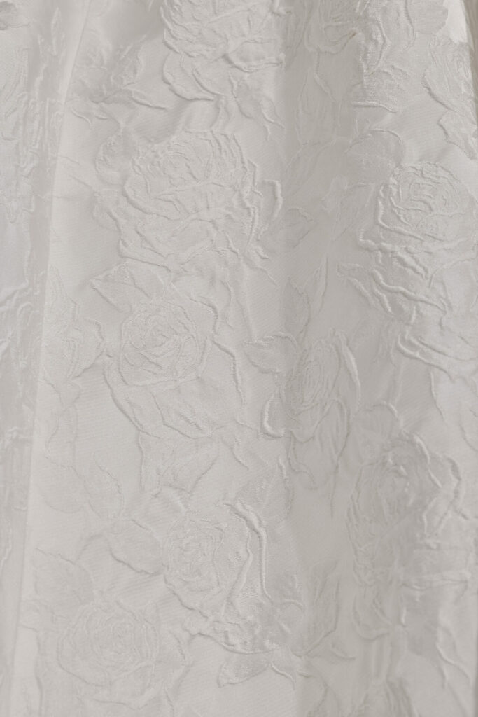 Shiny white fabric embossed with roses and leaves.