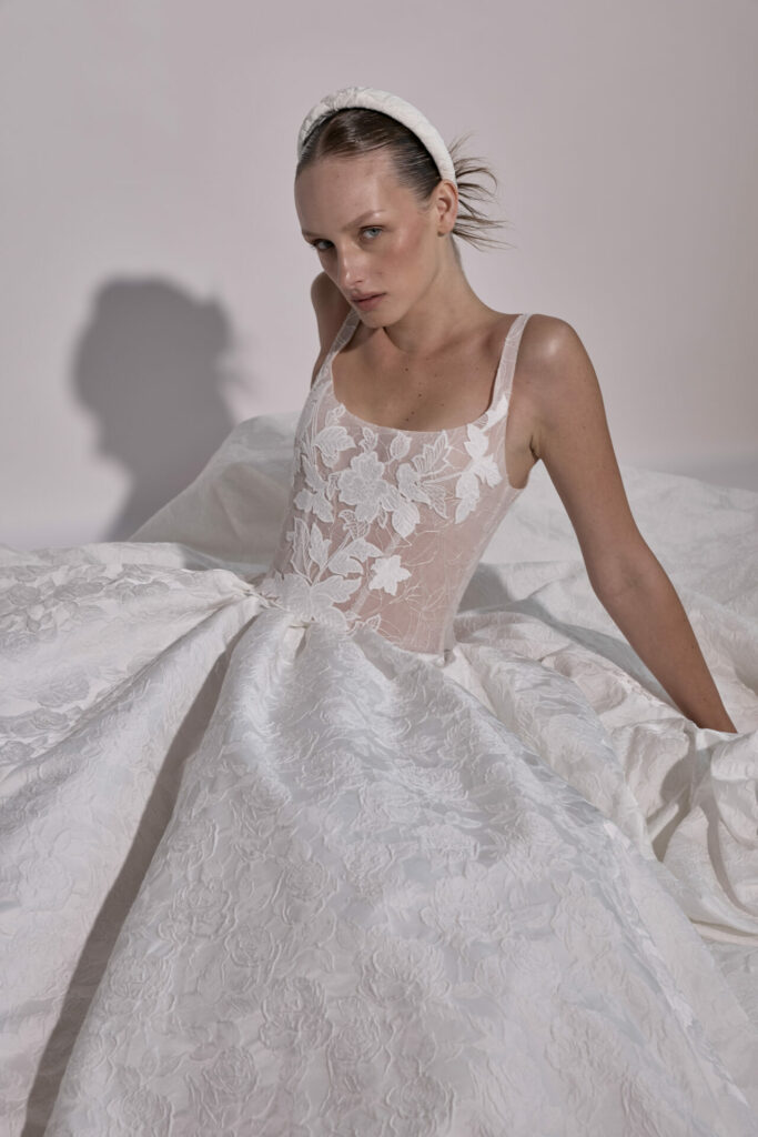 Woman in white lace gown, seated, facing camera.