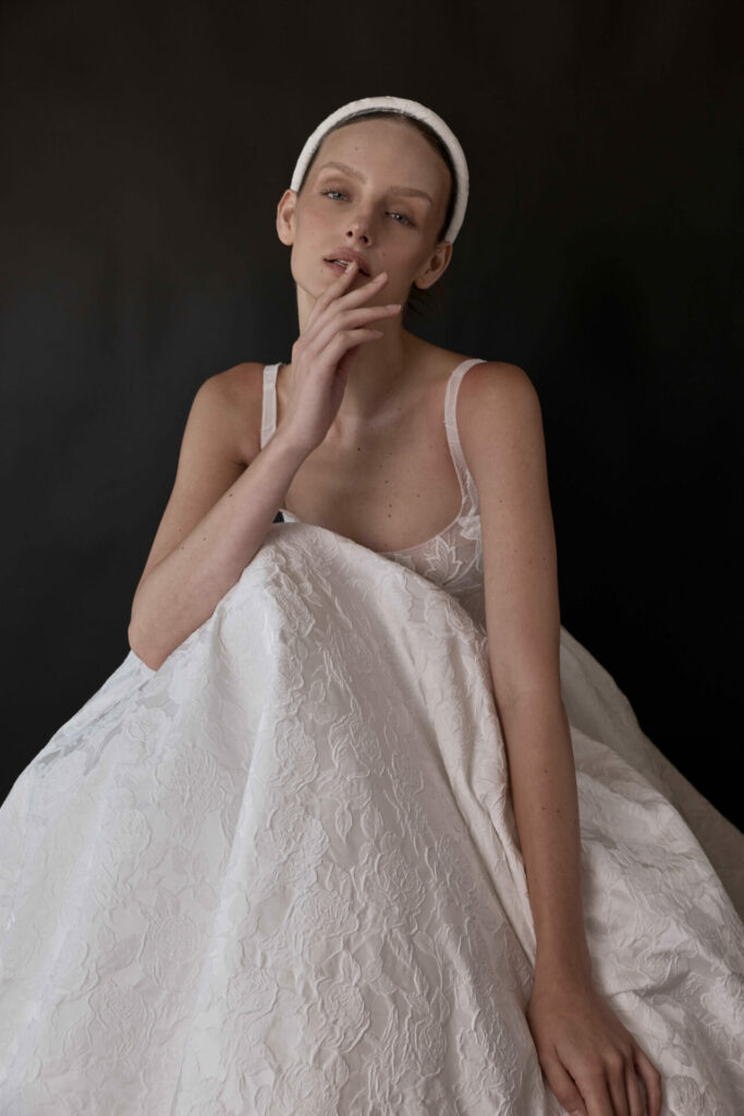 Woman in white dress poses thoughtfully against dark background.