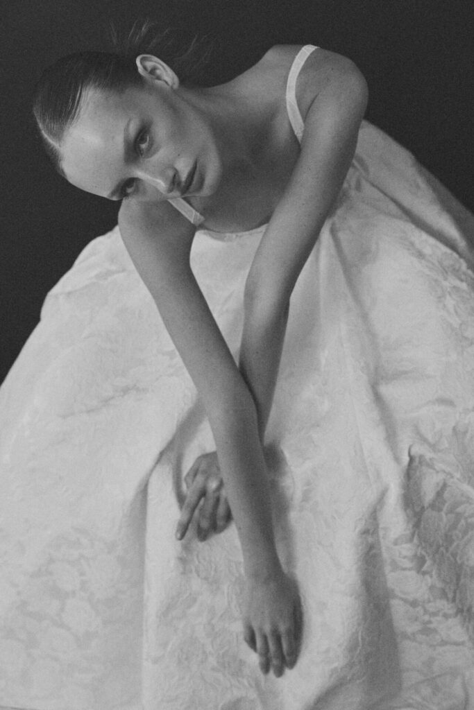 Woman in textured dress poses gracefully, soft B&W photo.