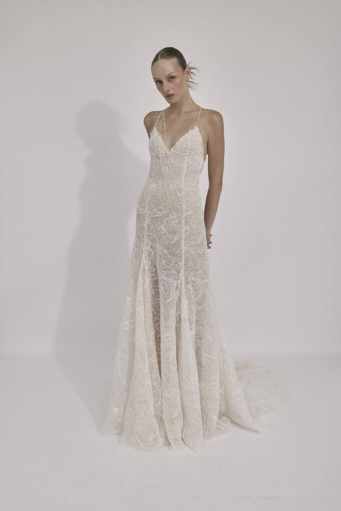 Woman in white lace gown poses against white background.