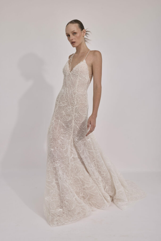 Woman in white lace gown poses confidently.