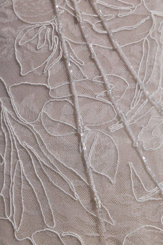 White embroidery, beaded lines on sheer pink fabric.
