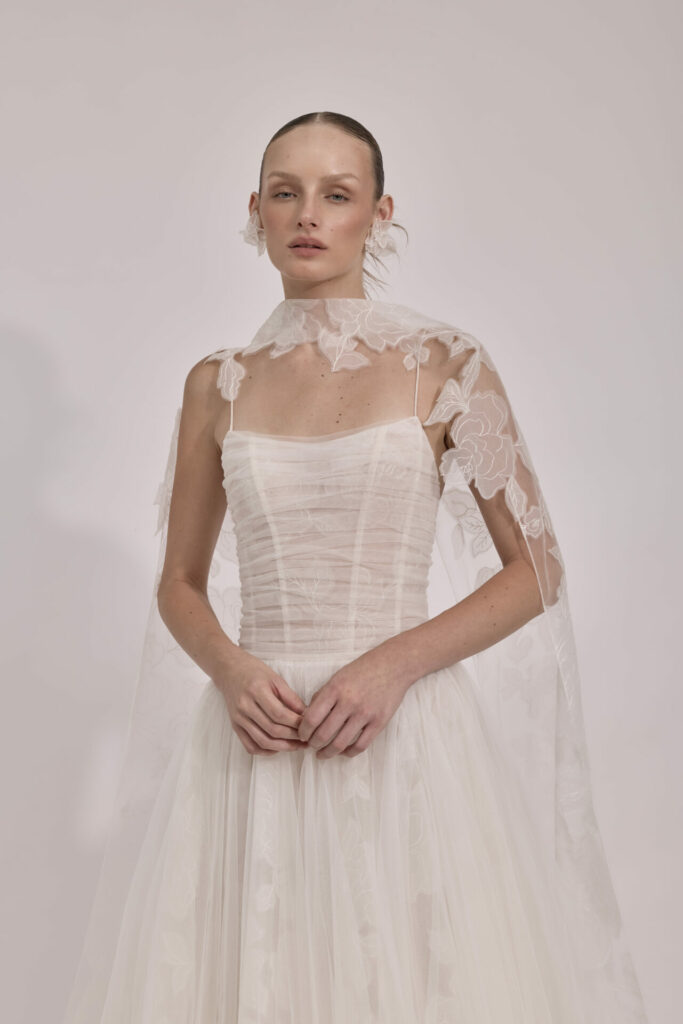 Woman in sheer embroidered wedding dress and cape.
