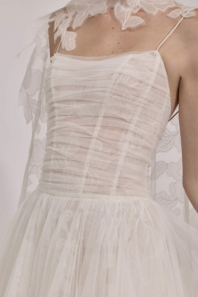 Woman in sheer white dress with floral embroidery.