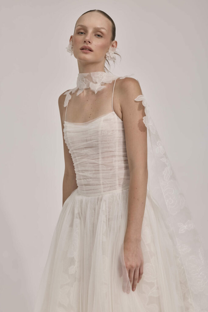 Woman in sheer white wedding gown with floral details.
