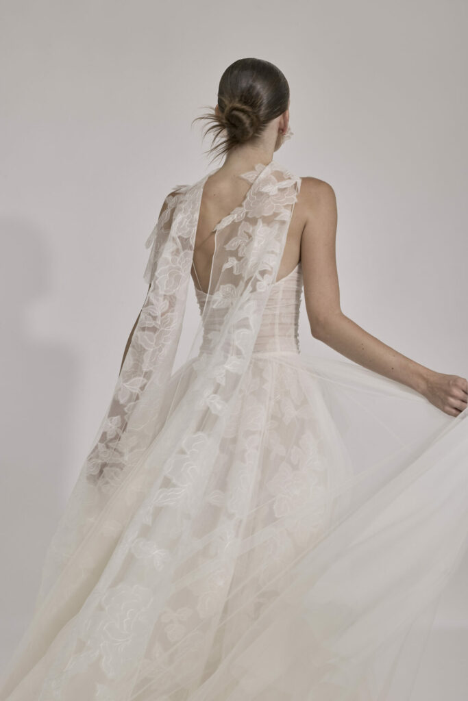 Woman in sheer floral gown, low bun, from behind.