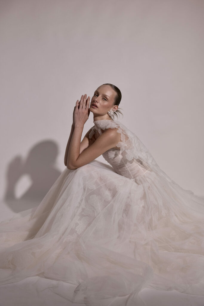 Woman in sheer white gown sits calmly, hands raised.