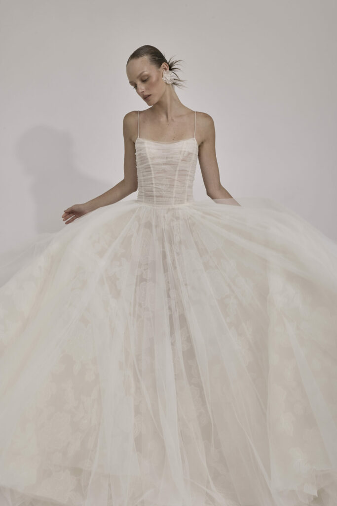 Woman in sheer white wedding gown holding skirt.
