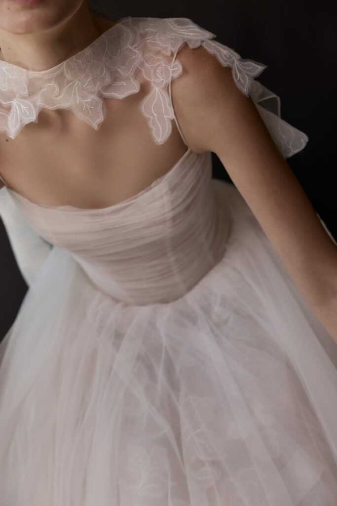Woman in sheer white floral wedding dress, dark background.