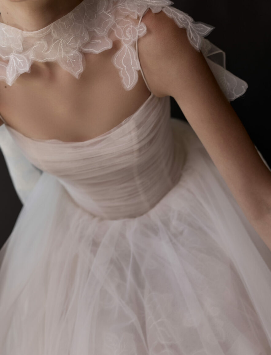 Woman in sheer white floral wedding dress, dark background.