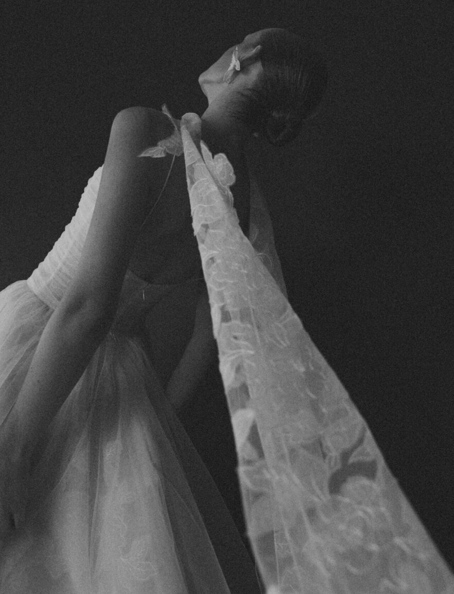 Person in white gown and veil, dramatic pose, monochrome.