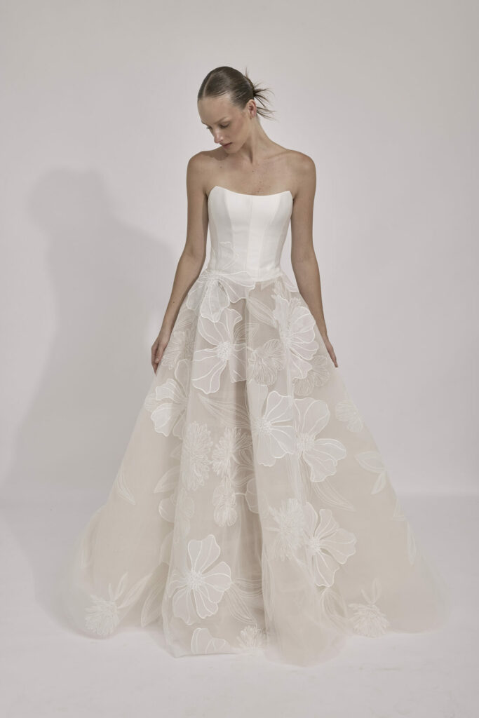 Woman in strapless white floral gown looks down.
