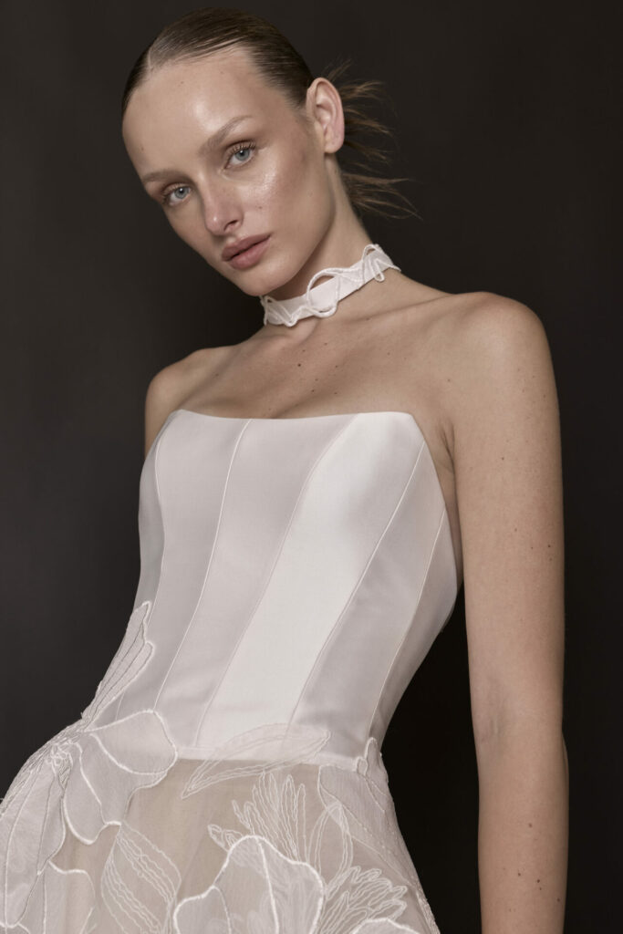 Woman in strapless white floral dress, dark background.