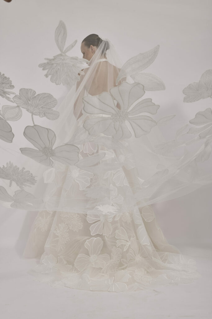 Bride in white gown, floral veil, back turned.
