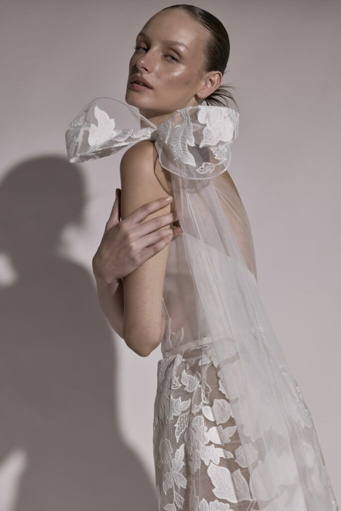 Woman in sheer floral gown with tulle bow.