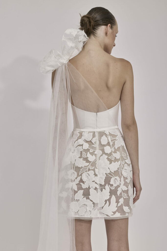 Woman in white lace dress, sheer bow, low bun.