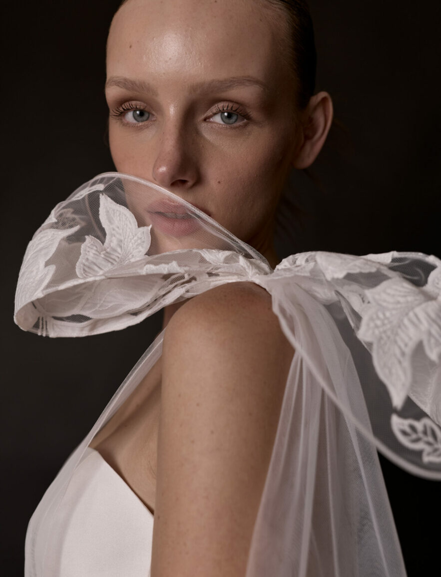 Woman in sheer white Mira Zwillinger dress posing.