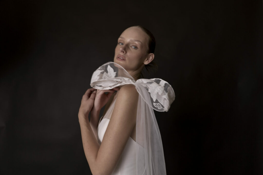 Woman in white dress, floral bow, glances back.