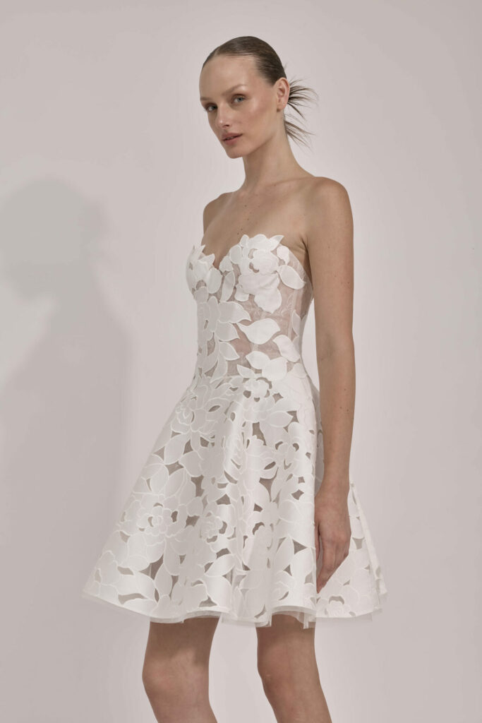 Woman in white strapless floral dress, plain background.