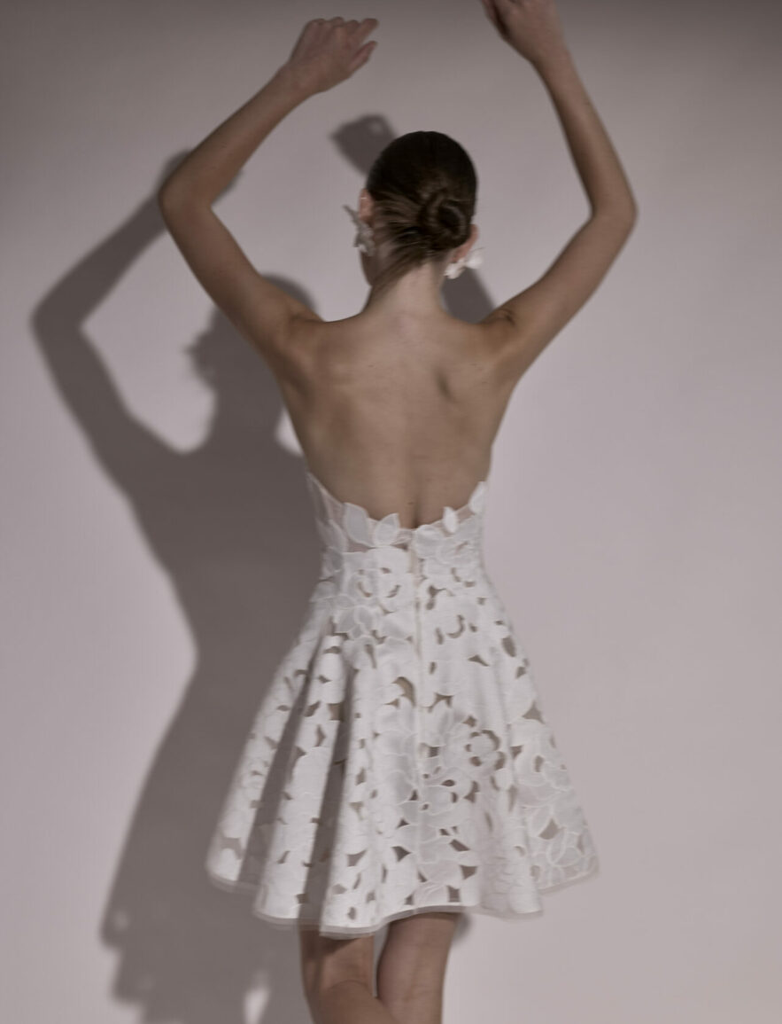Woman in strapless dress raises arms, shadow behind.