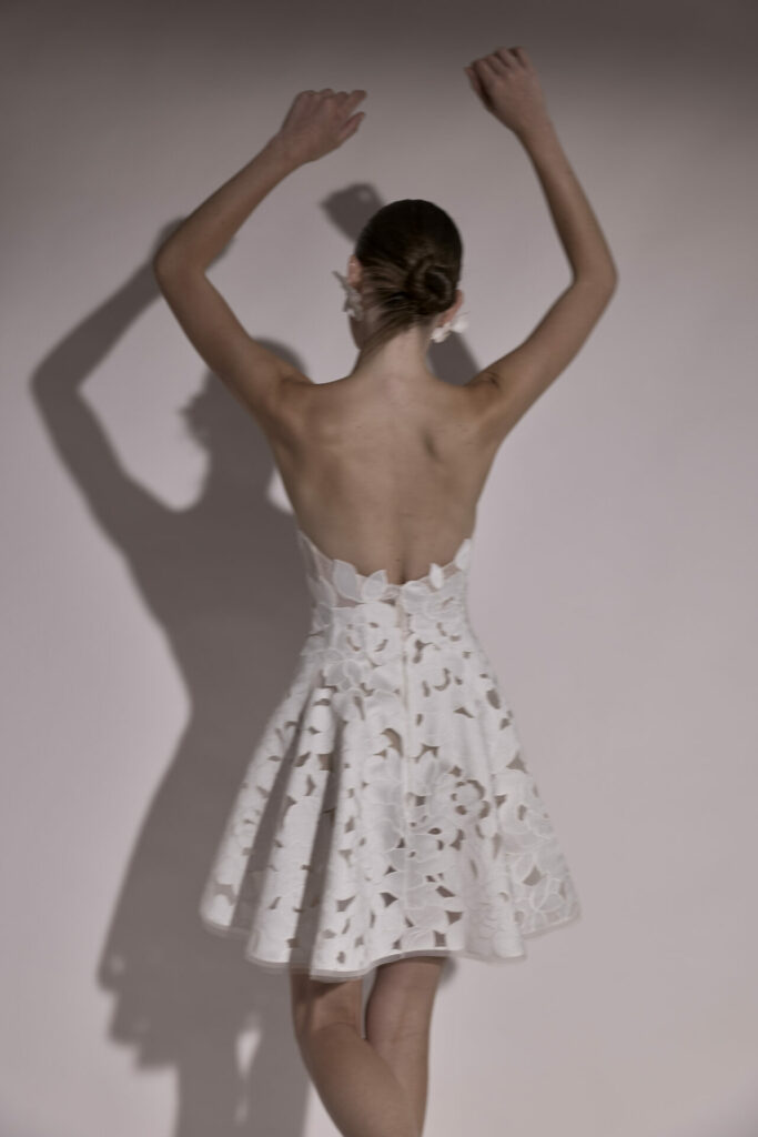 Woman in strapless floral dress stands, arms raised.