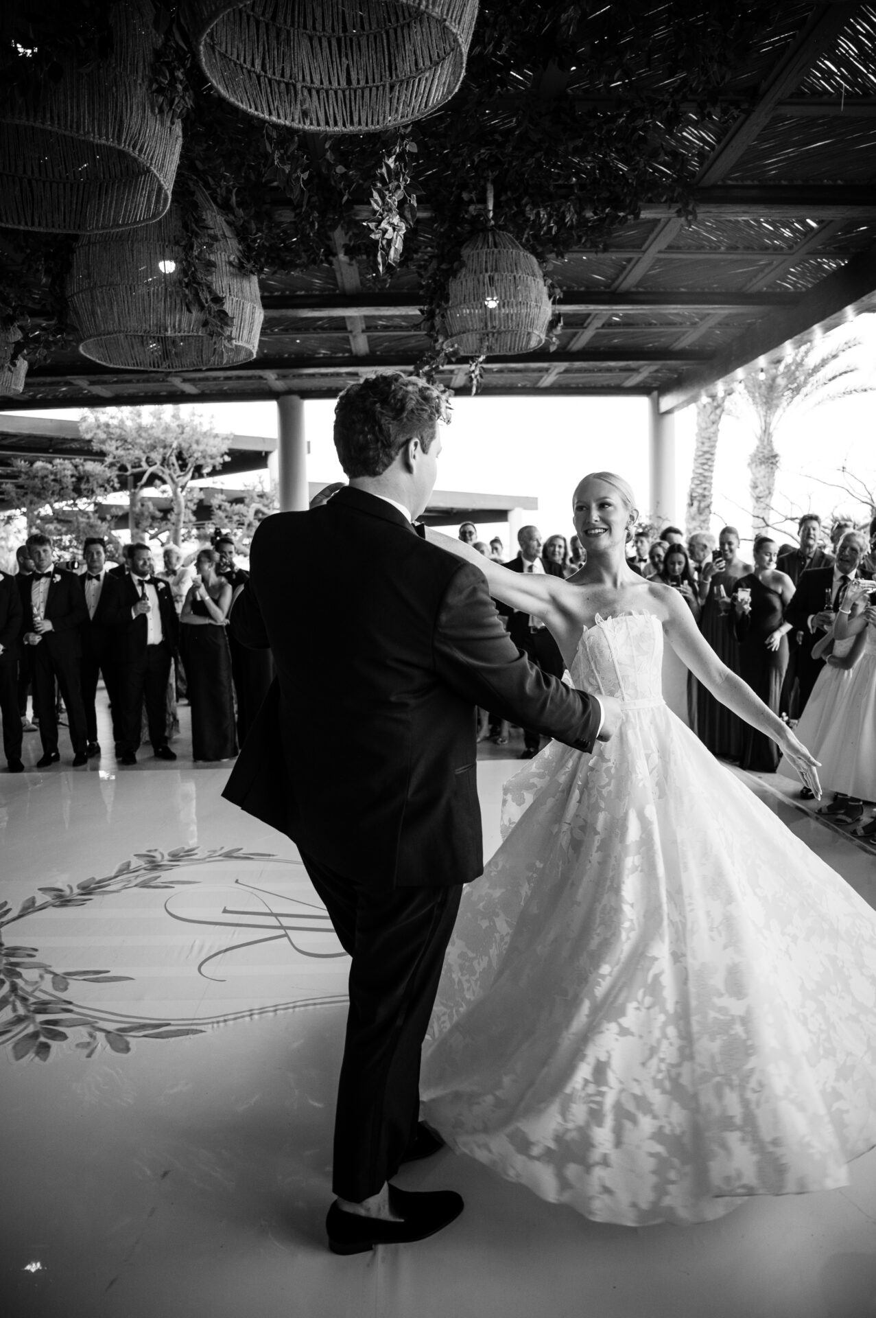 Bride and groom dance on decorated floor, guests watch.