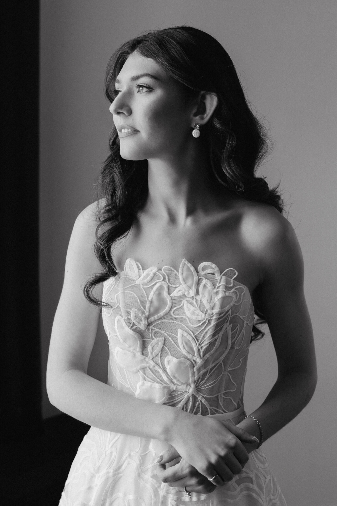 Thoughtful woman in strapless dress by window, grayscale.