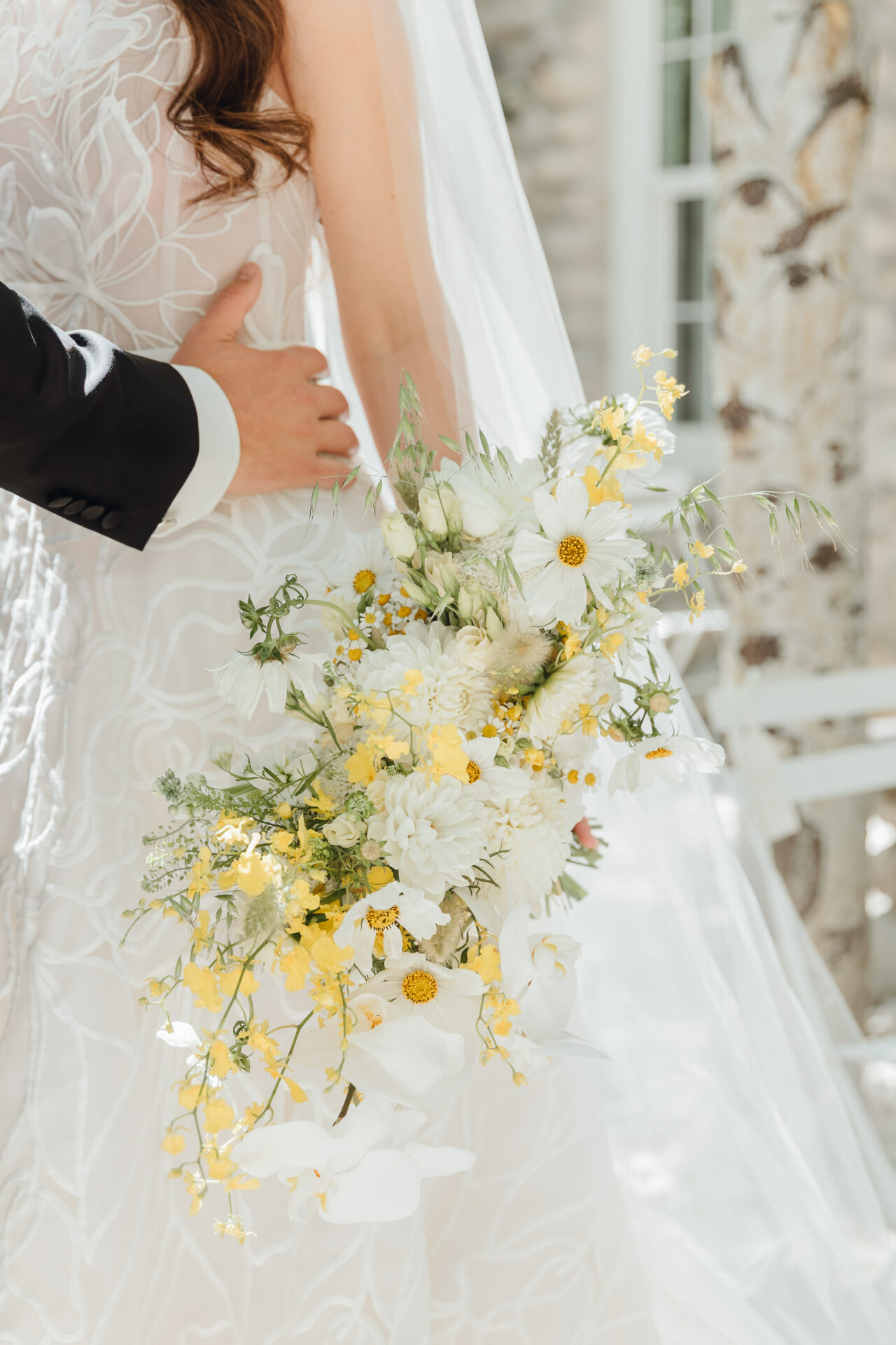 Bride and groom embrace in sunlight with bouquet.