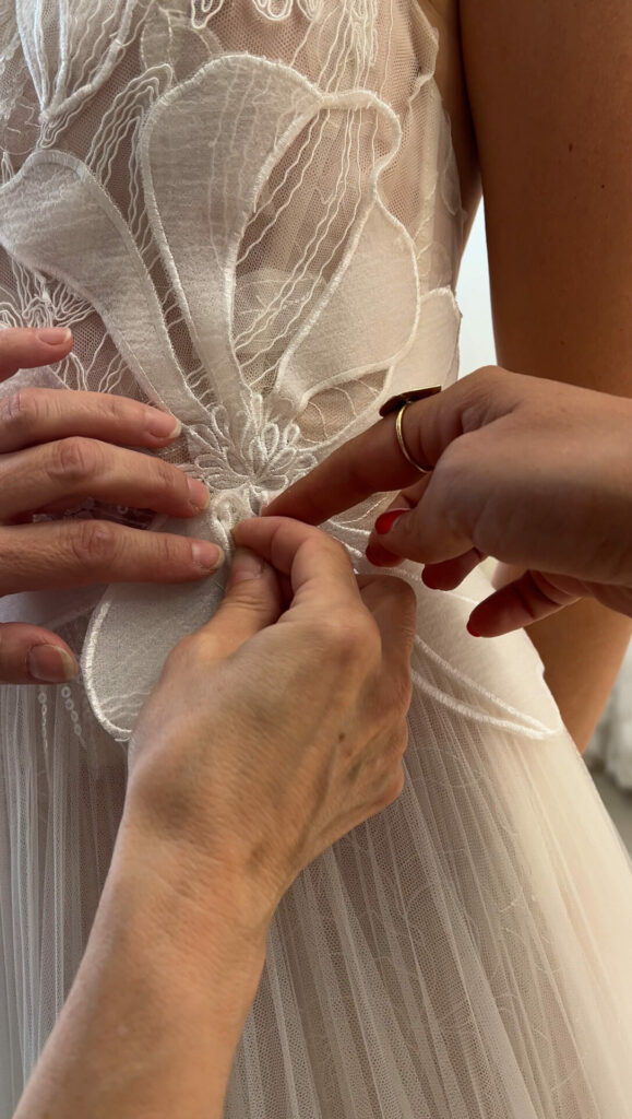 Hands fasten lace buttons on modern bridal gown.