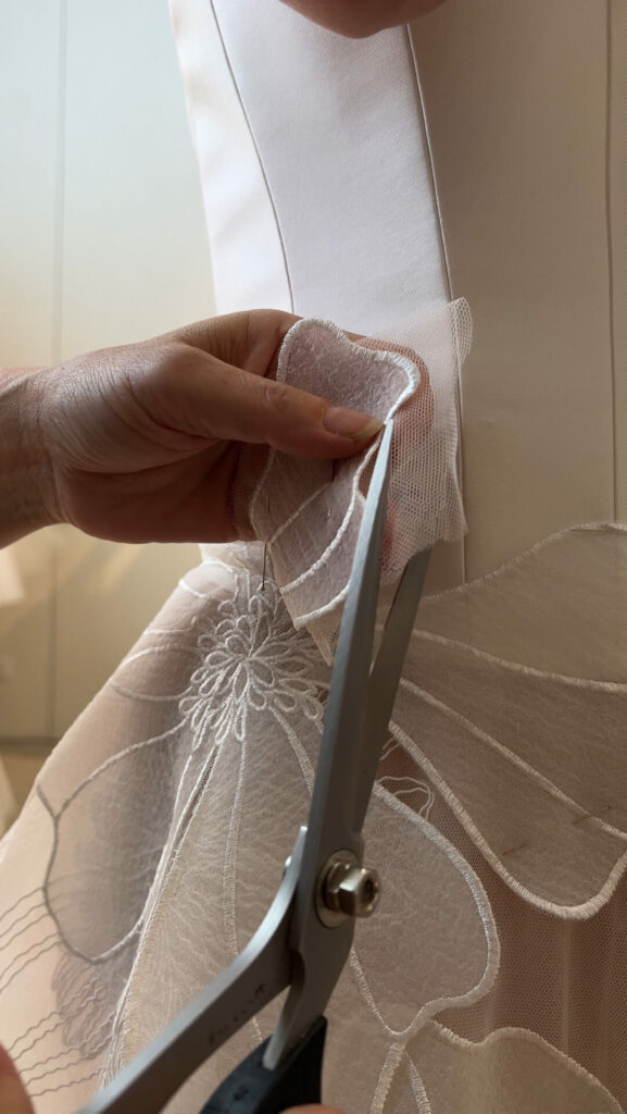 Hands trimming embroidered tulle fabric with scissors.