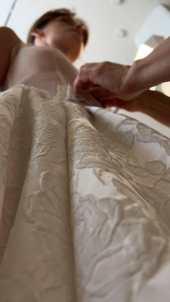 Hands adjust waist of elegant white ball gown.